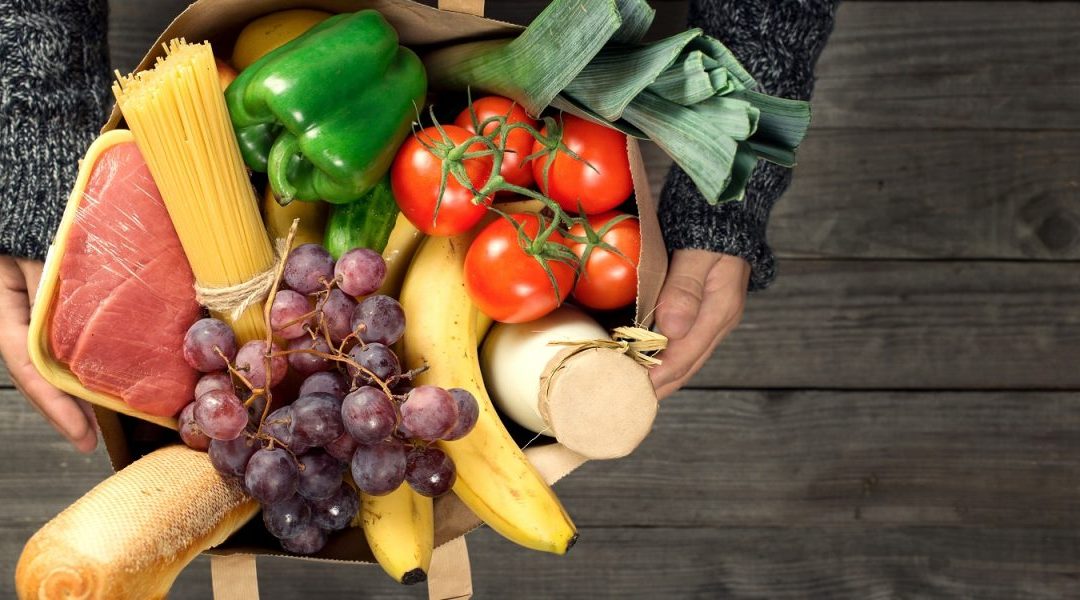 Grocery bag with tomatoes, grapes, bananas, corn, green peppers, and meat.