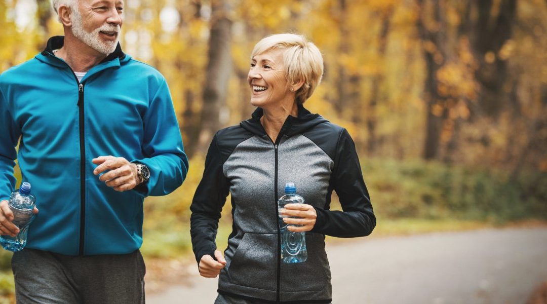 Senior couple running outside in a wooded path.